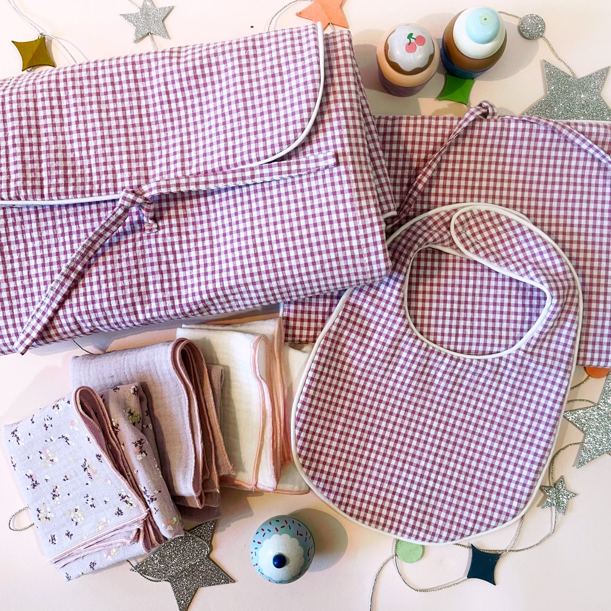 Conjunto de cambiador de paseo en estampado de cuadros rosa claro y blanco junto con el babero y el porta toallitas de estampado cuadros rosa y blanco ; juego de tres muselinas en color malva con flores, malva liso y color blanco liso con acabados en hilo rosa