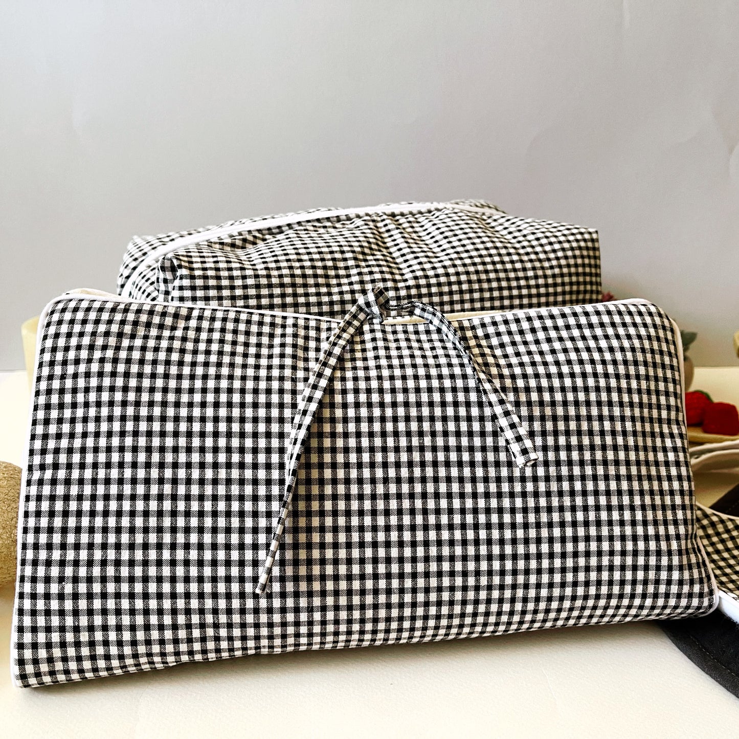 Conjunto frontal del porta toallitas en estampado de cuadros blanco y negro cerrado con dos lazos y detrás el neceser de la misma tela