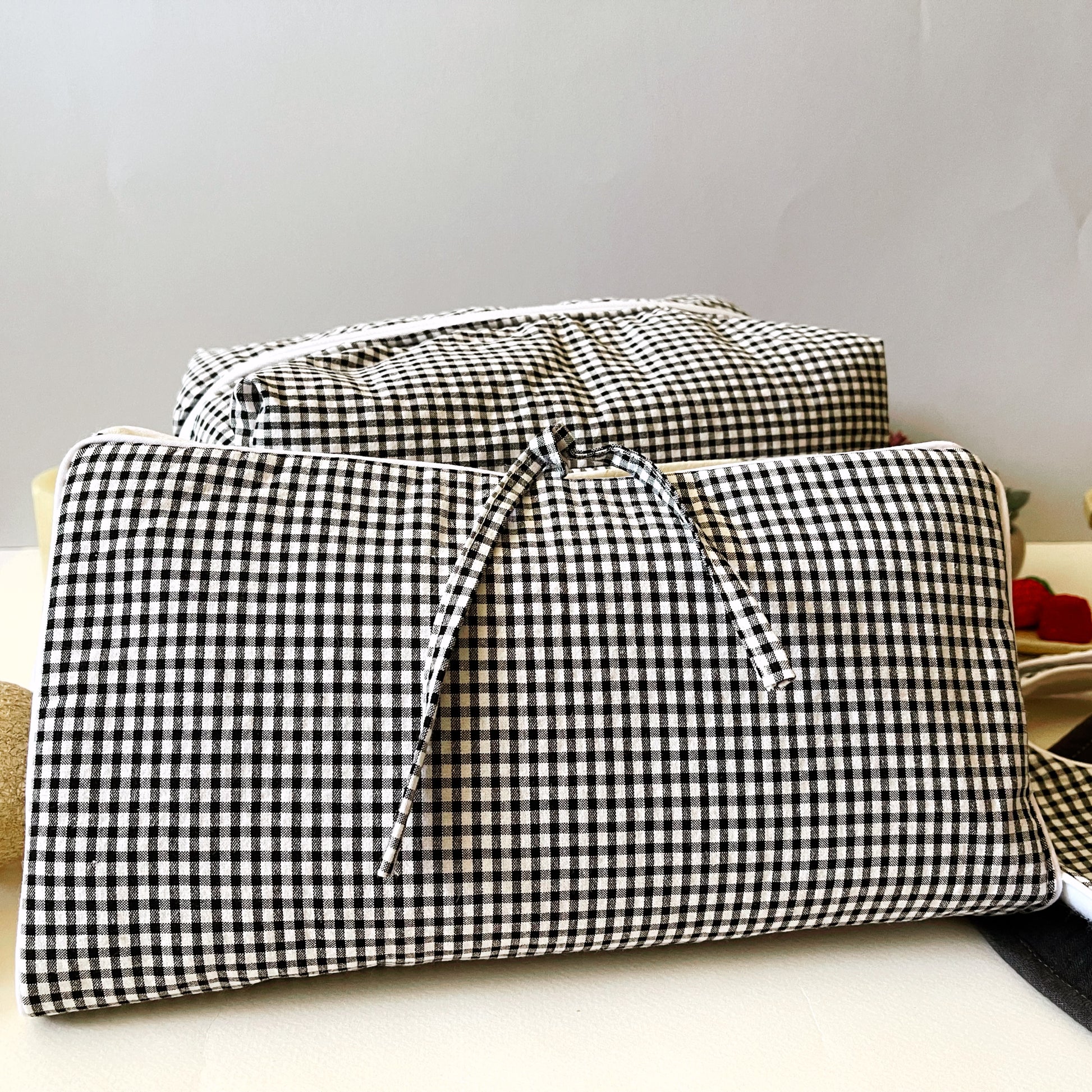 Conjunto frontal del porta toallitas en estampado de cuadros blanco y negro cerrado con dos lazos y detrás el neceser de la misma tela